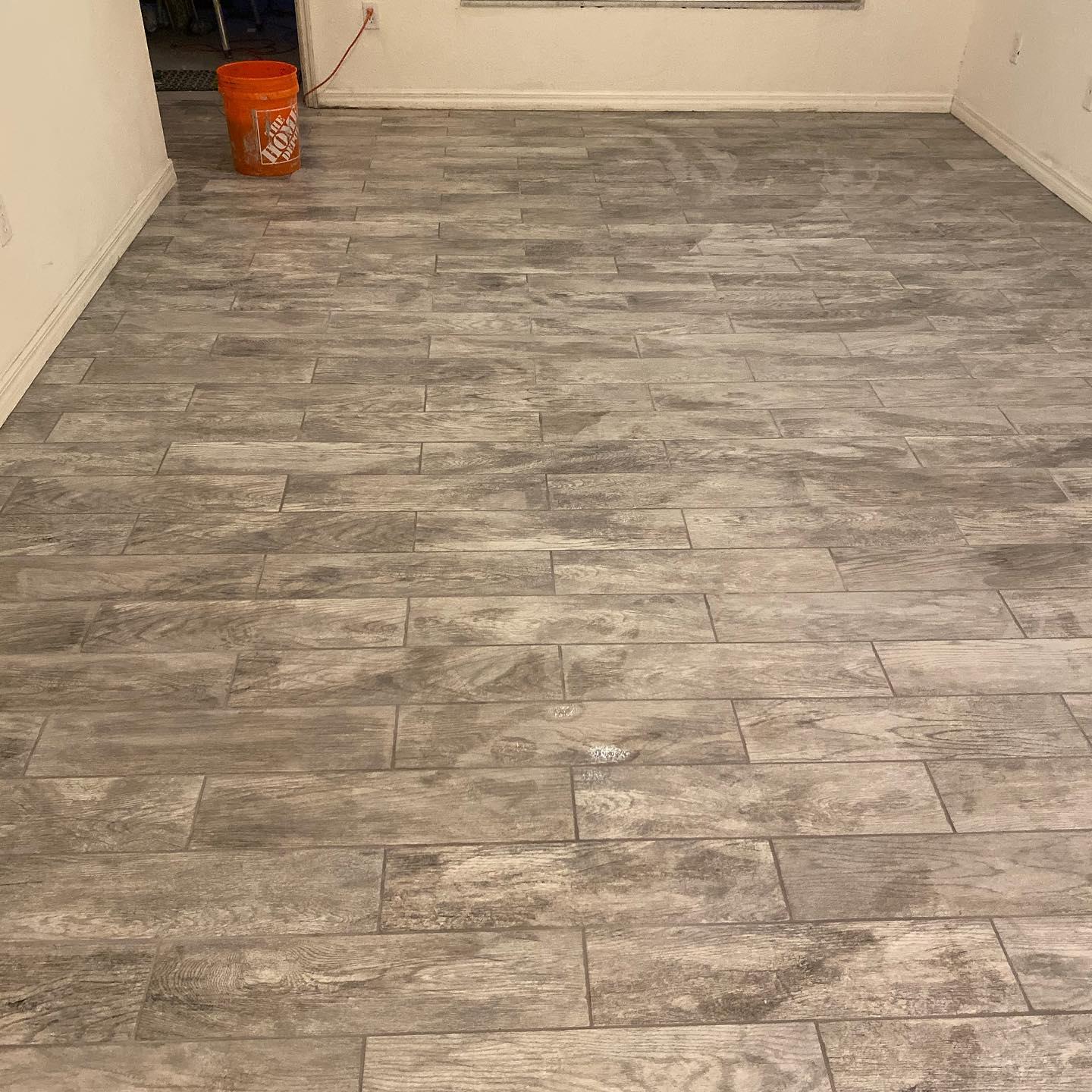 Gray wood-look tile flooring in an empty room, orange bucket in the corner.