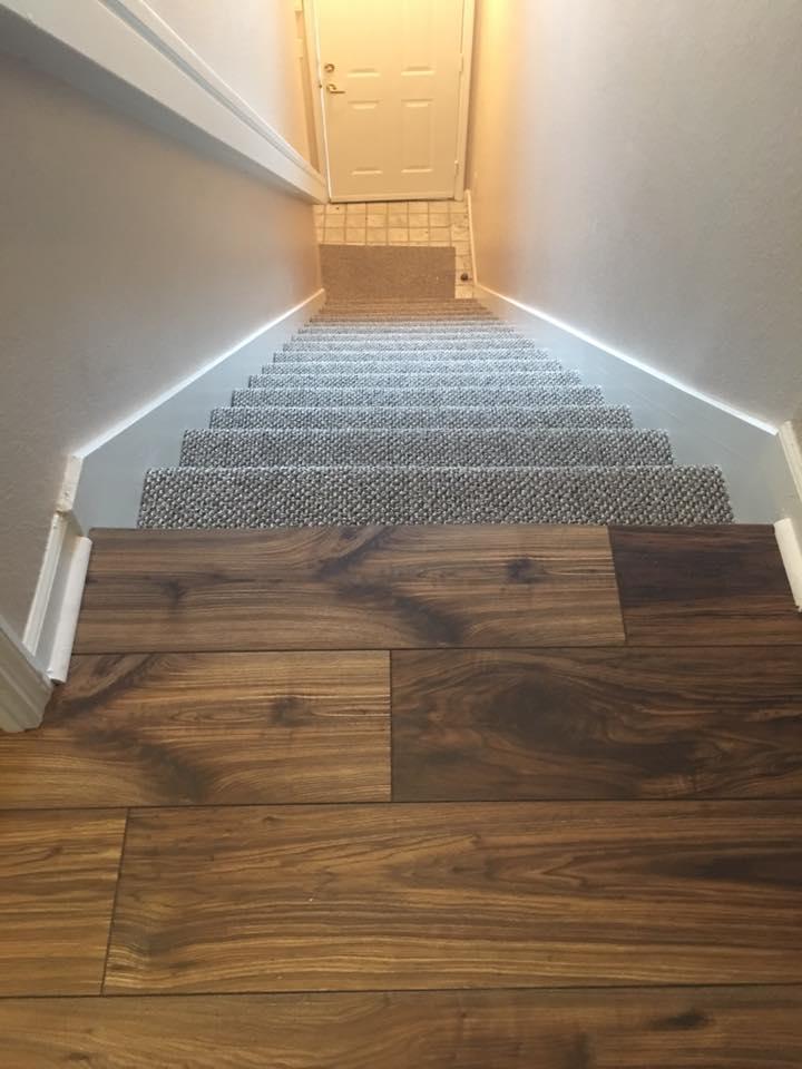 Staircase with wood flooring transitioning to carpeted steps, leading up to a closed white door.