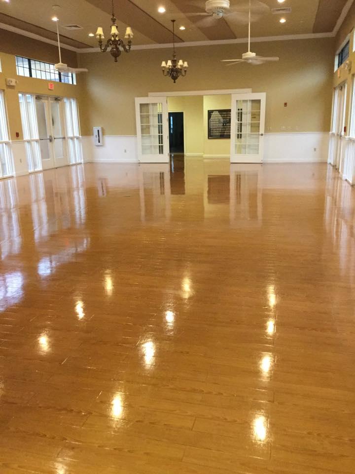 Empty ballroom with glossy wooden floor, chandeliers, and white doors.
