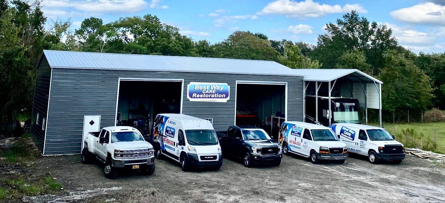 A business storefront with a fleet of vans and trucks, with a sign in front of a metal building.