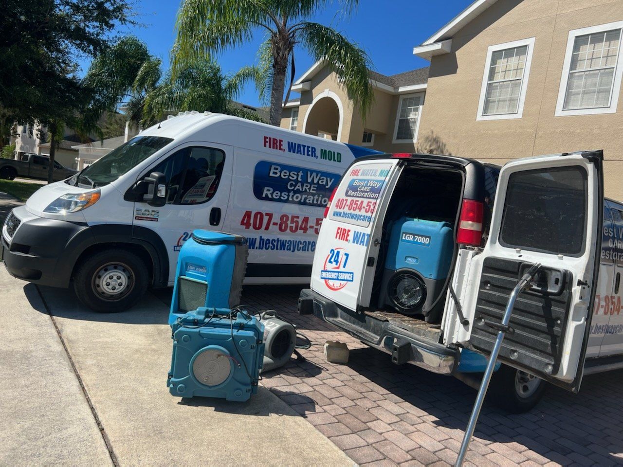 Two restoration vans with equipment parked in front of a house. One van is open, revealing a dehumidifier.