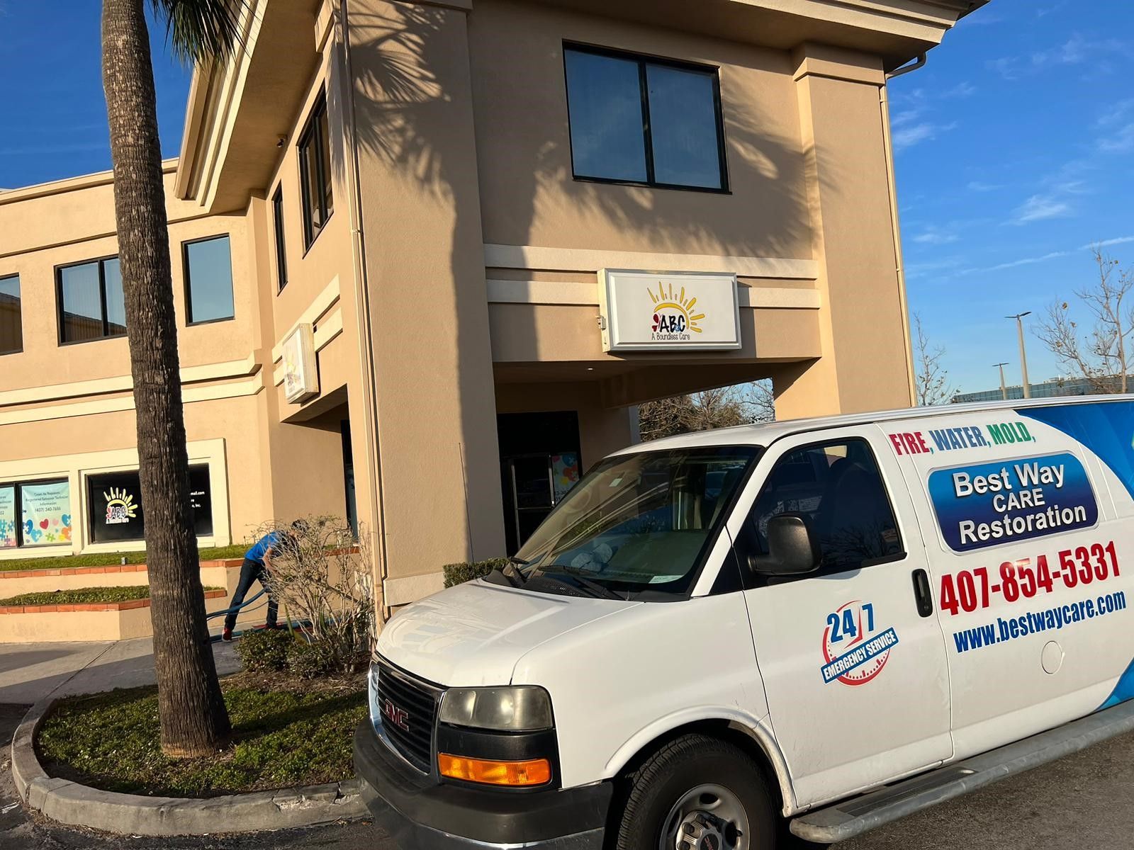 White van parked outside a beige office building, a person outside and a sign with a sun.