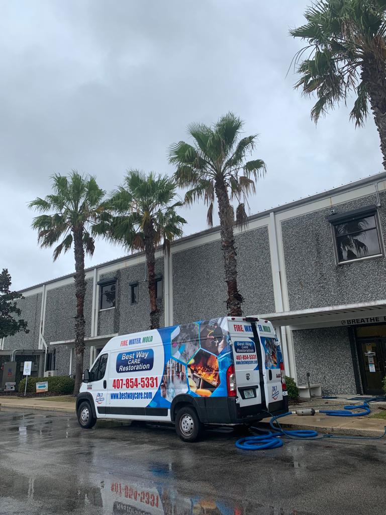 A white service van parked outside a building on a cloudy day, with palm trees.