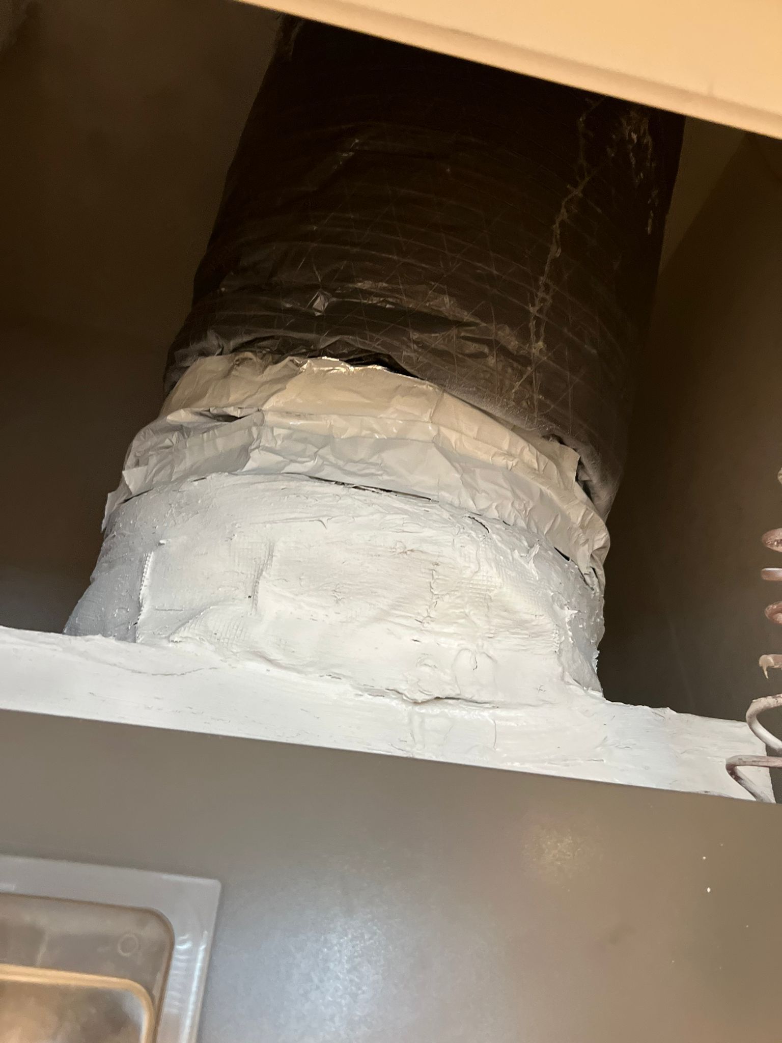 Flexible ductwork connected to a rectangular opening, sealed with white caulk.
