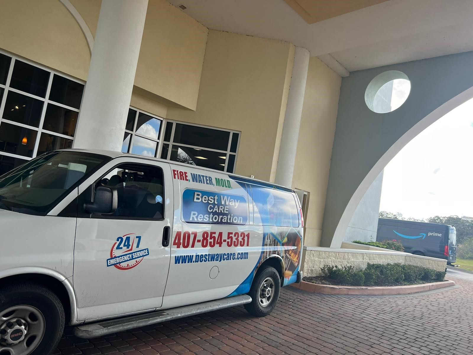 White van with company logo parked near building entrance; another van is visible in the background.