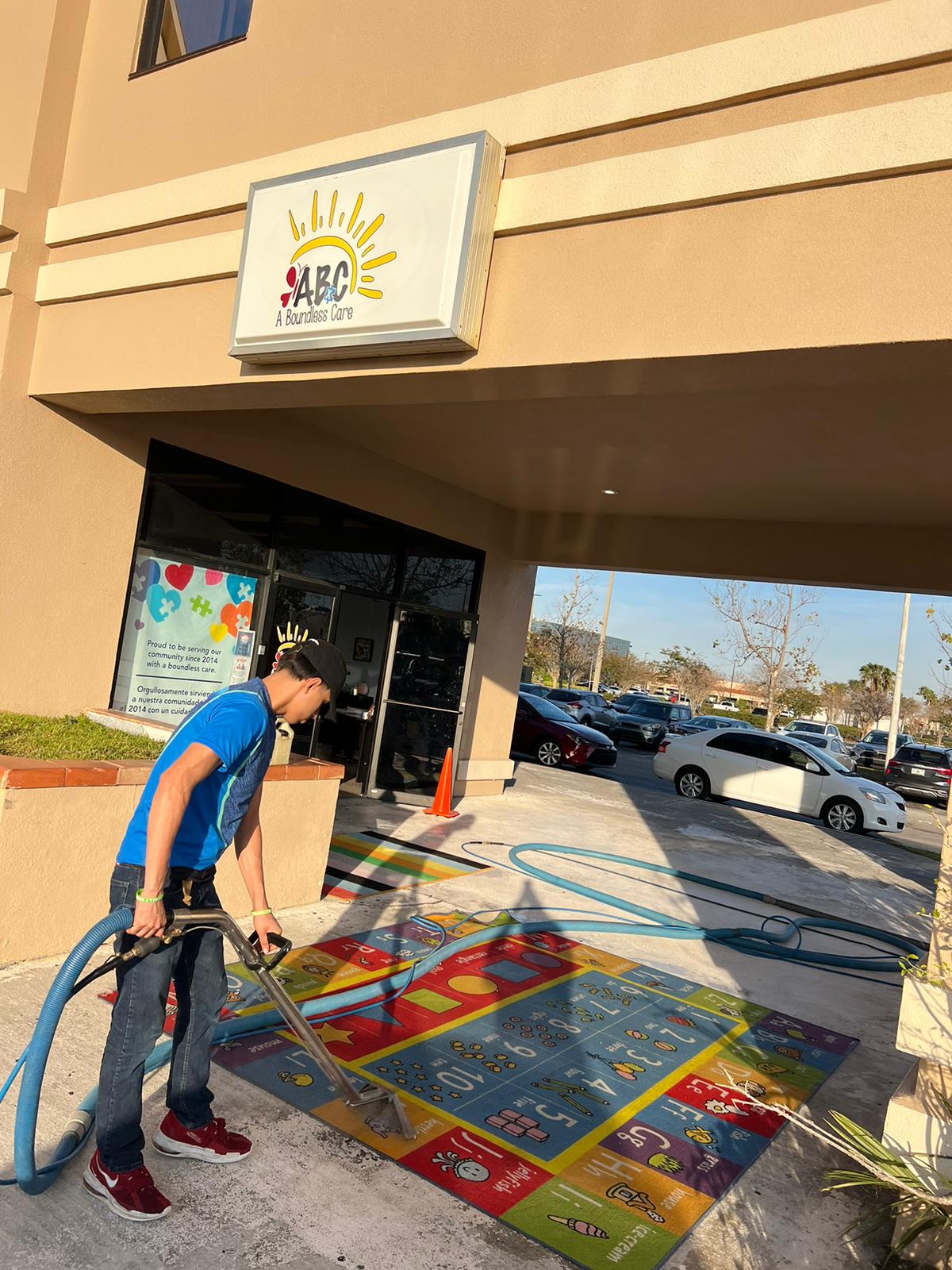Man cleaning a colorful rug outside a building with the 
