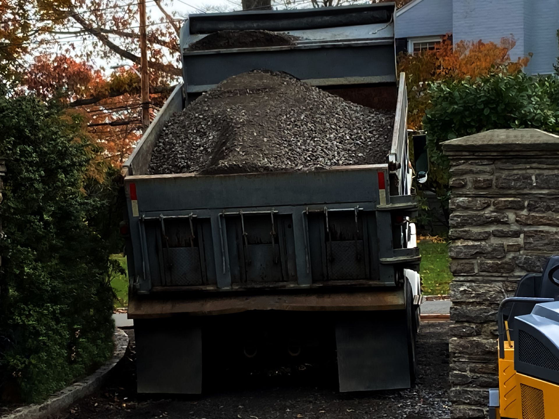 A Dump Truck Filled with Gravel Is Parked in Front of A Stone Wall — Paving Contractors In Butler, PA A Dump Truck Filled with Gravel Is Parked in Front of A Stone Wall — Paving Contractors In Butler, PA