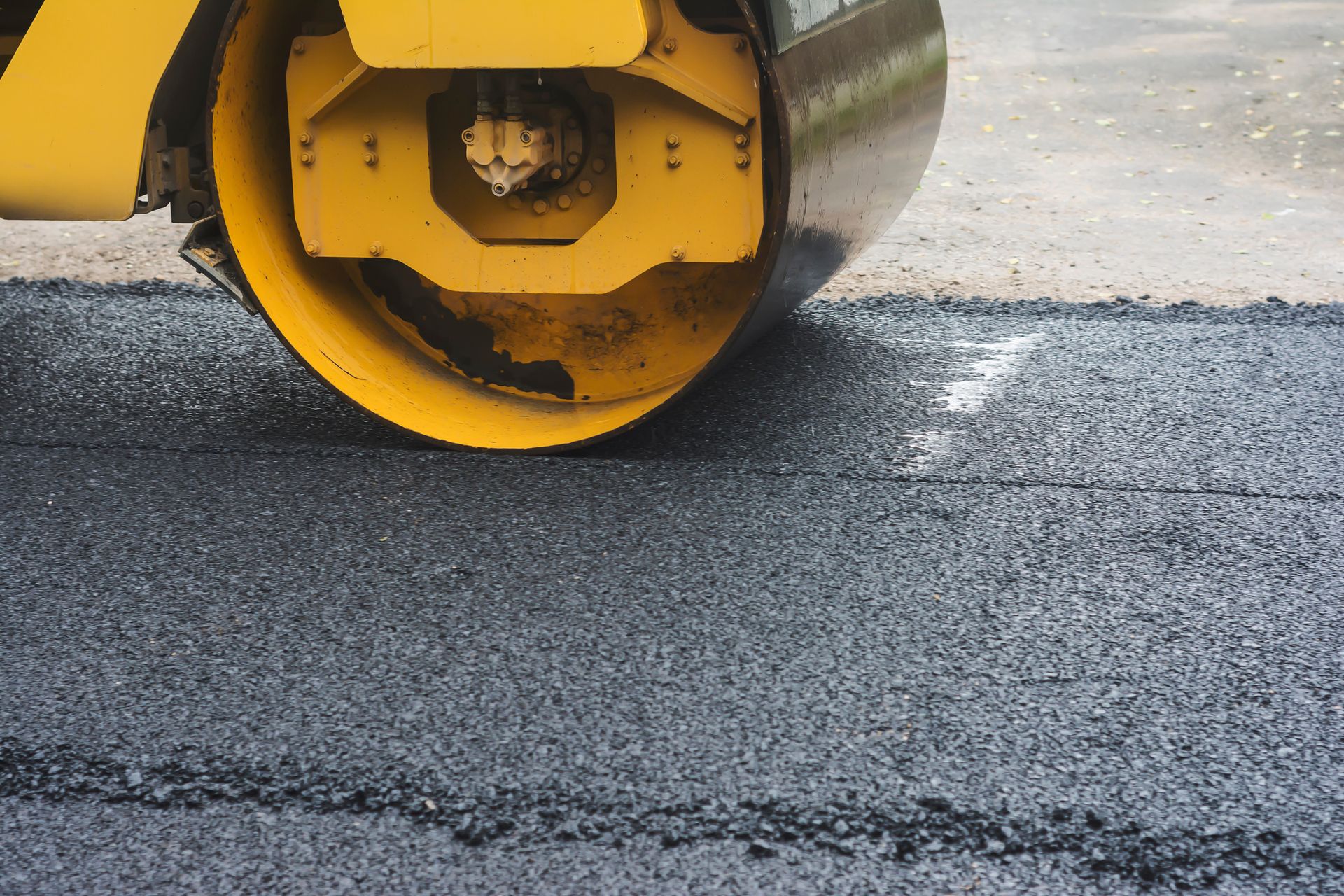 A Yellow Roller Is Rolling Asphalt on A Road — Paving Contractors In Butler, PA a yellow roller is rolling asphalt on a road .