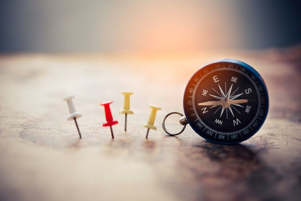 Compass beside four colorful push pins on a softly blurred surface with warm light