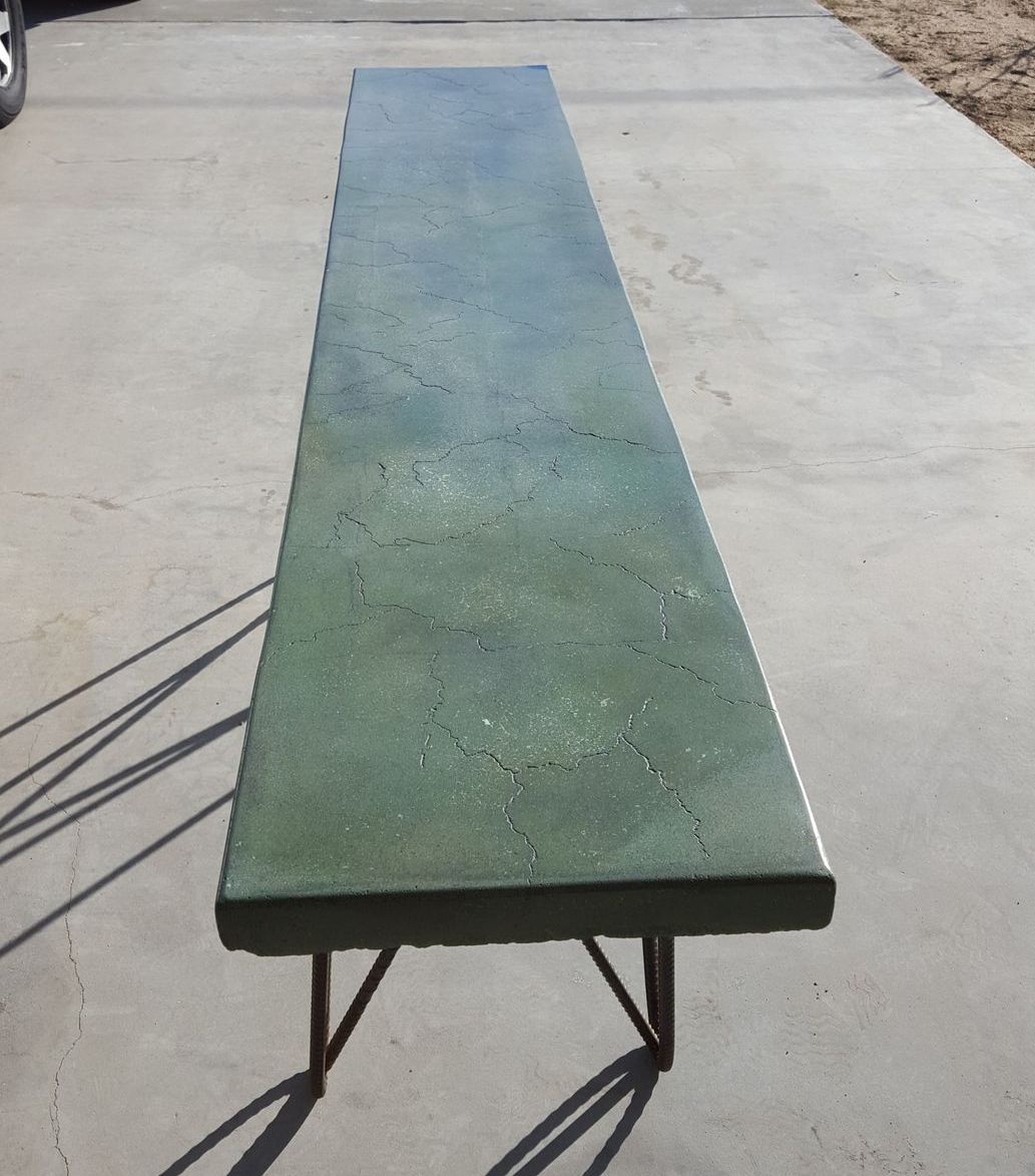 A long green bench is sitting on a concrete driveway