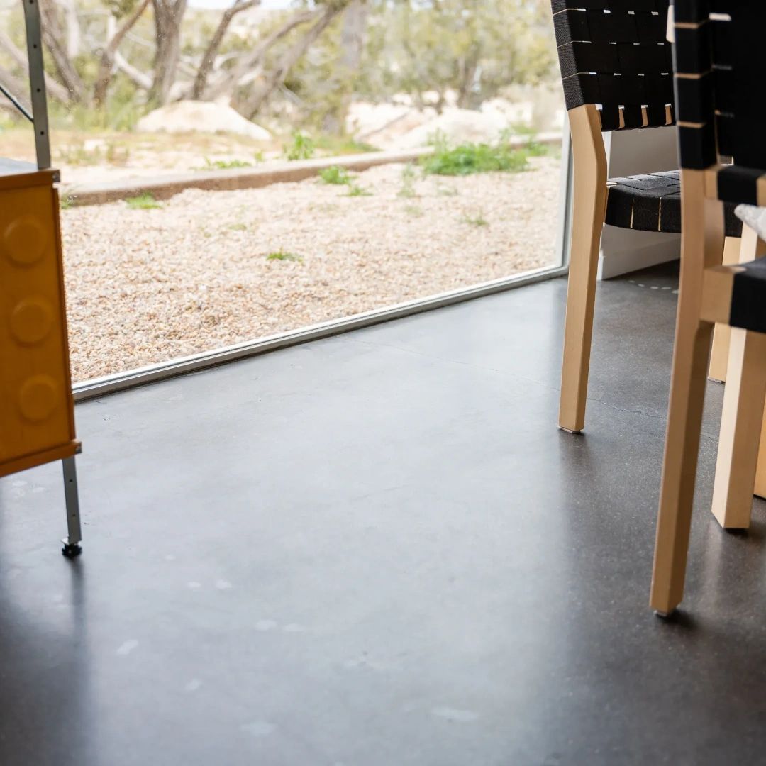 A table and chairs in a room with a large window, all on a polished concrete floor.