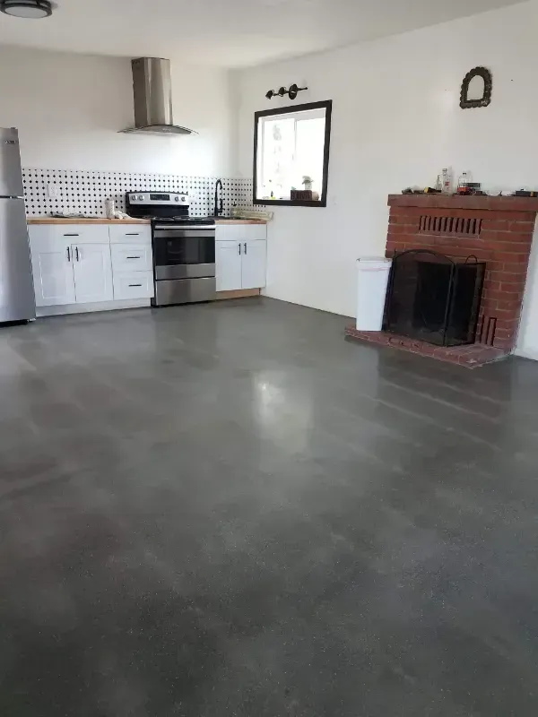 A room featuring a kitchen with white cabinets, stainless steel appliances, and a red brick fireplace on gray floors.