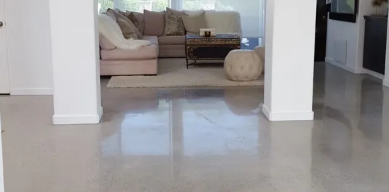 Bright living room with a beige sofa, coffee table, round ottoman, and glossy tiled floor viewed through a doorway