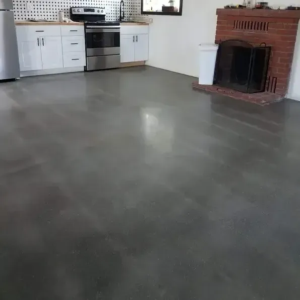 A modern kitchen with white cabinets, stainless steel appliances, and a red brick fireplace on a smooth gray concrete floor.