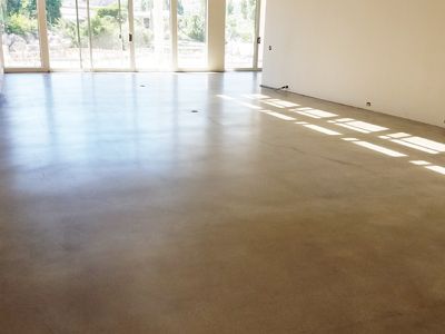 Polished concrete floor in an empty room, natural light streaming through large windows, highlighting the sheen.