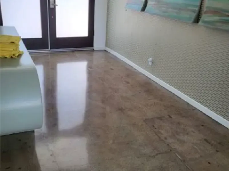 Polished concrete floor in an office hallway with white baseboards and a decorative wall feature near a doorway.