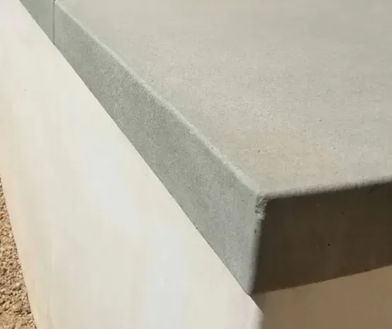 Close-up of a gray countertop edge with a smooth beveled corner against a white wall.
