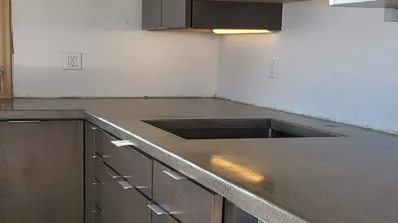 Modern kitchen with gray concrete-style countertops, dark cabinets, a center island with stools, and pendant lighting.