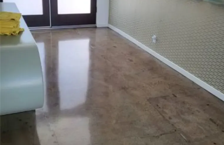 Empty room with polished brown floor, white walls, and glass doors at the far end.