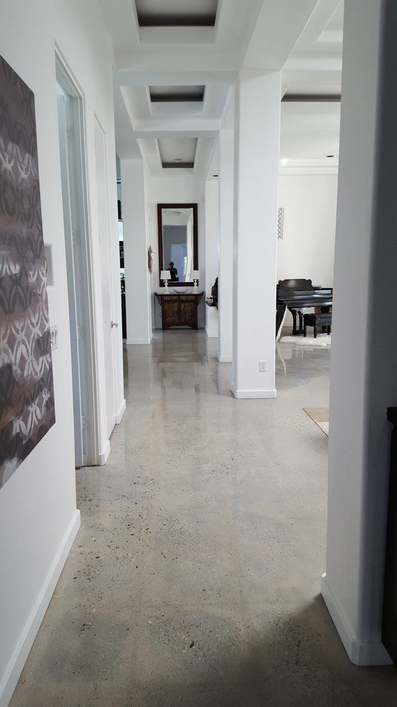 A hallway in a house with a painting, a mirror on the wall, and a polished concrete floor.