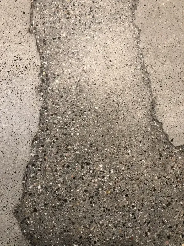 Gray, speckled concrete restoration on floor with large, irregular cracks.
