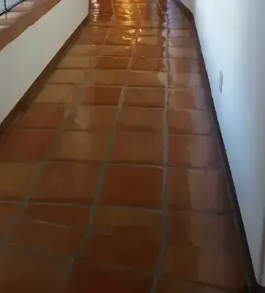 Narrow hallway with terracotta tile floor and white walls, viewed from one end.