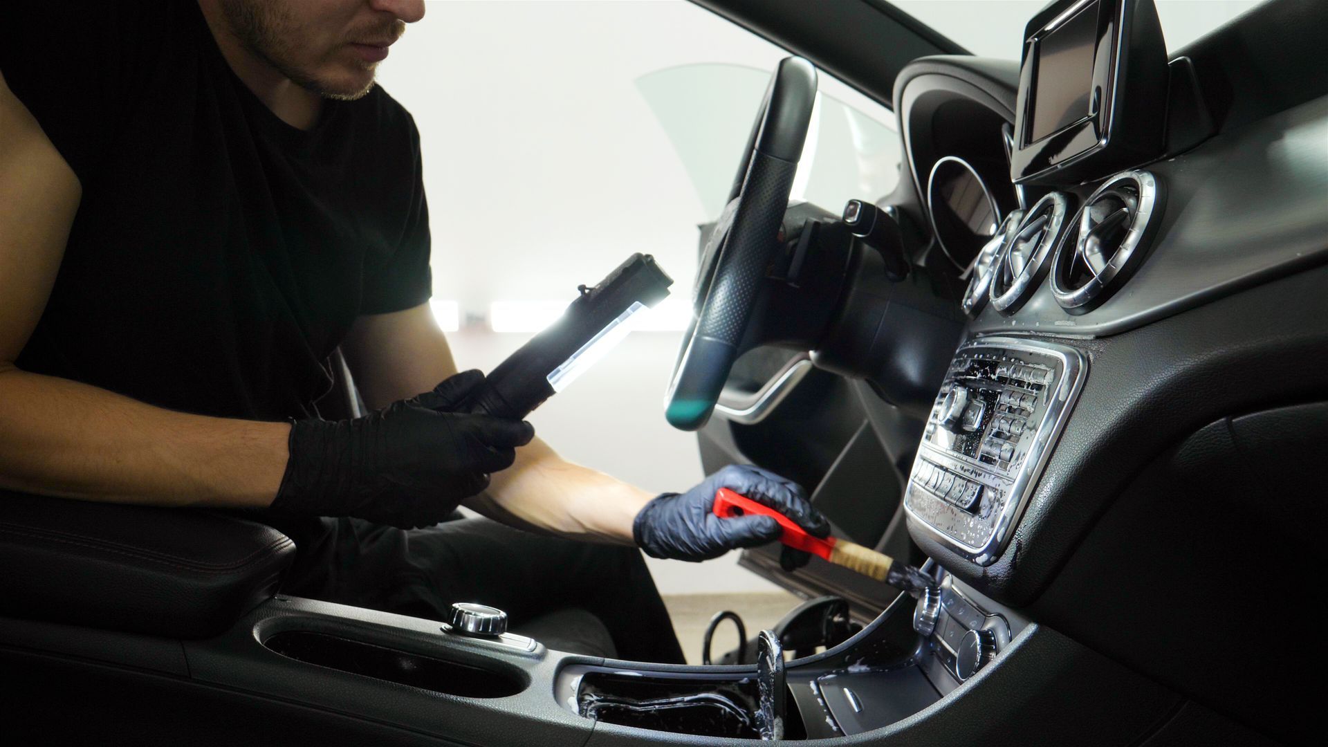 Man cleaning a car interior with a brush and flashlight.