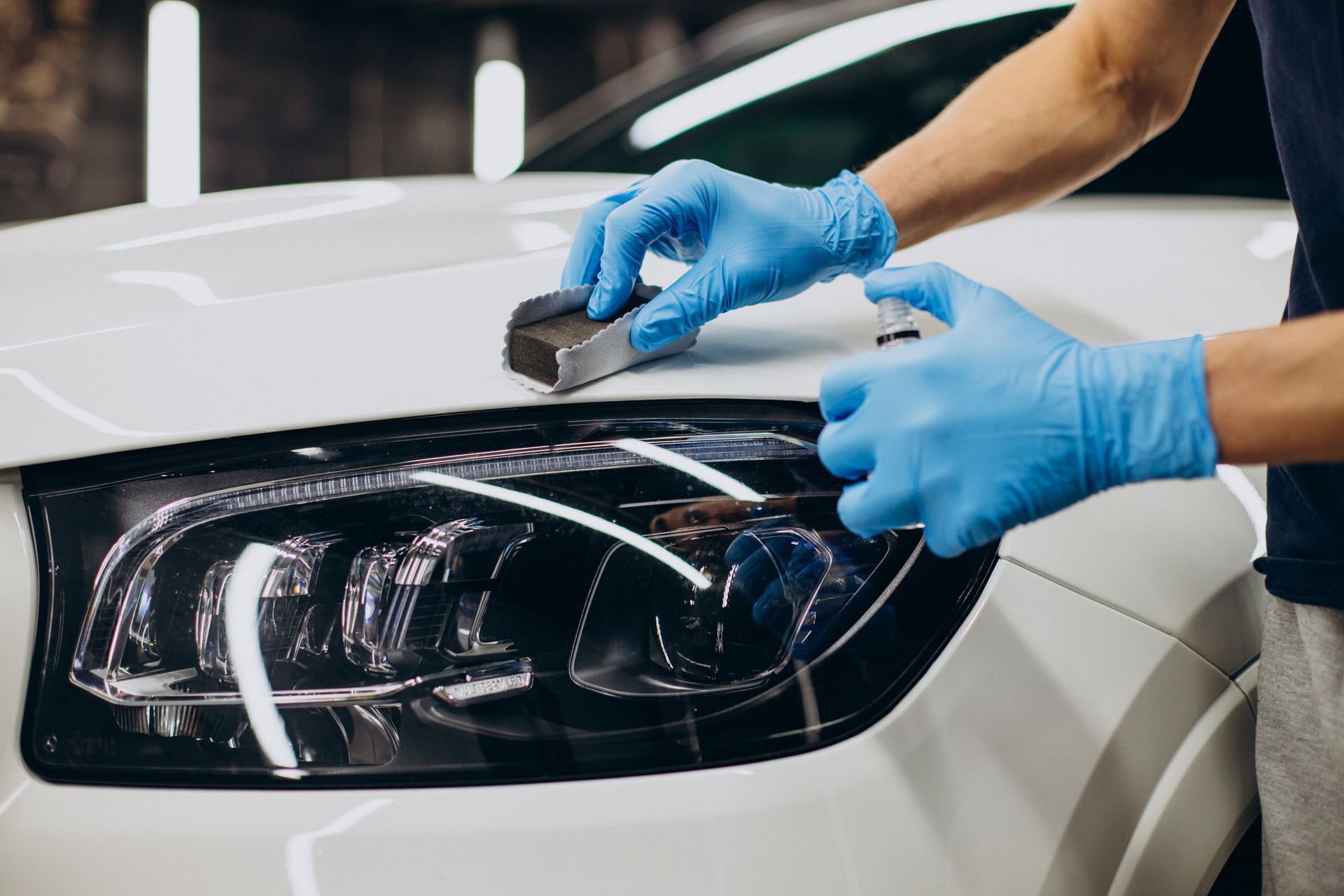 Person using a buffer to polish a black car's side, removing surface imperfections, in a garage.