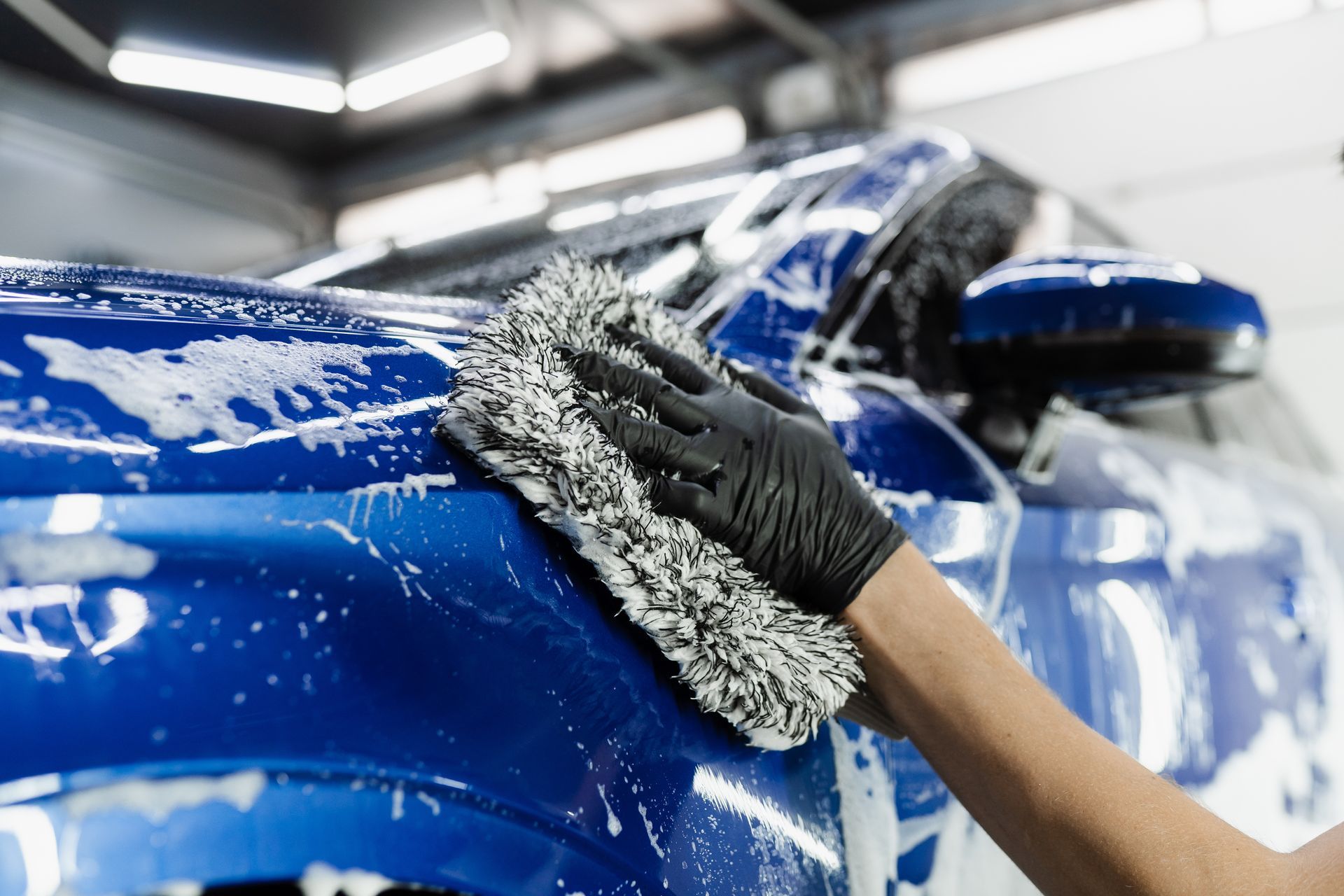 Person using a buffer to polish a black car's side, removing surface imperfections, in a garage.