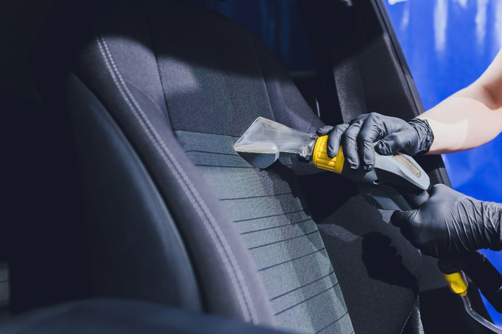 Man cleaning a car interior with a brush and flashlight.