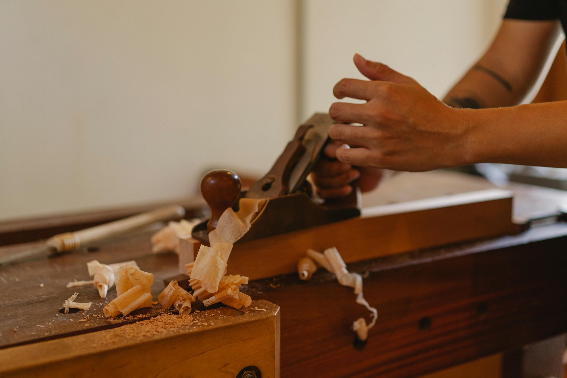 Hands planing wood on a workbench, shavings falling.