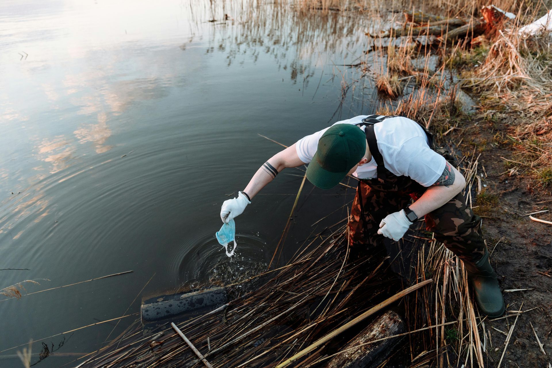 Person in waders picks up a discarded mask from a body of water.