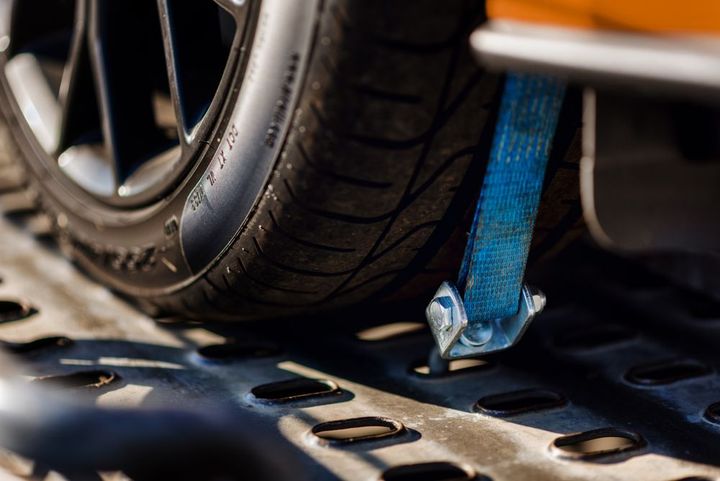 Car tire strapped to a flatbed trailer with a blue tie-down strap