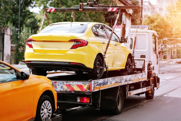 Yellow car on a tow truck with an orange car in front on a city street at sunset