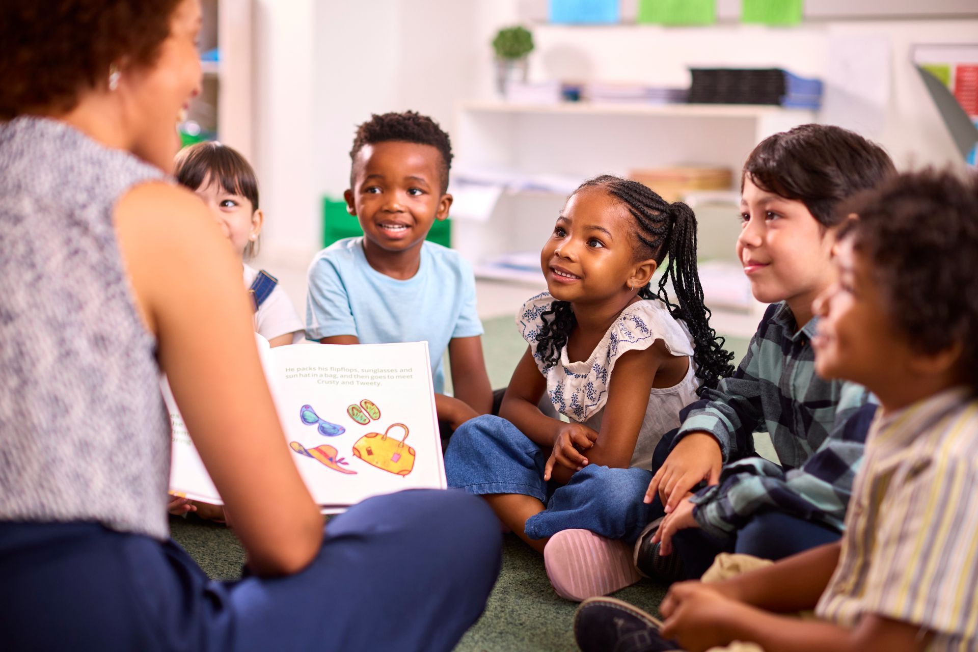 Teacher reading to a small group of children sitting on the floor in a classroom Teacher reading to a small group of children sitting on the floor in a classroom