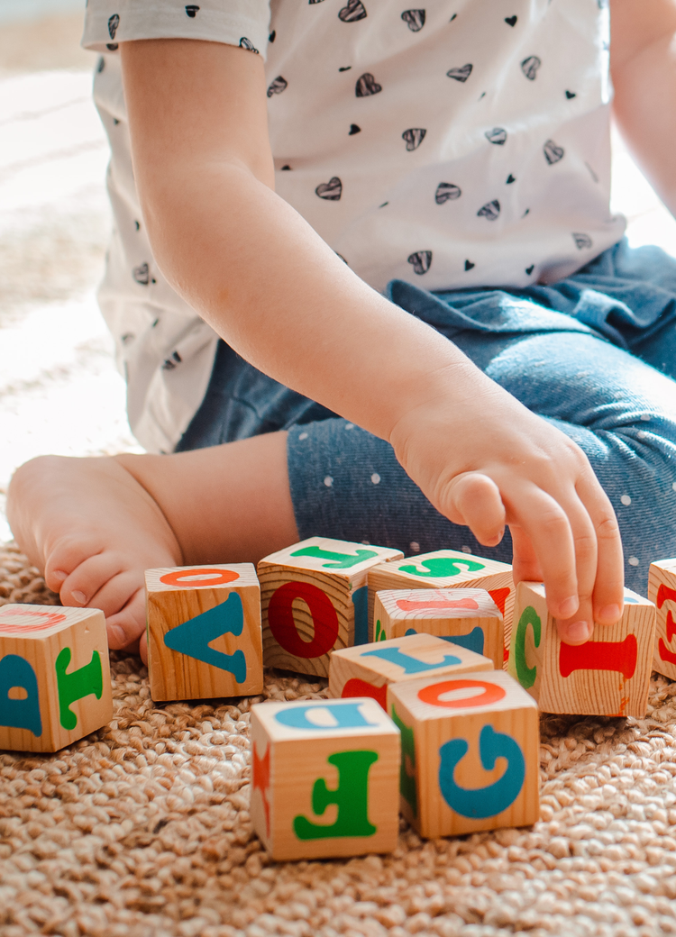 Child playing with colorful alphabet blocks on a woven rug in a bright room