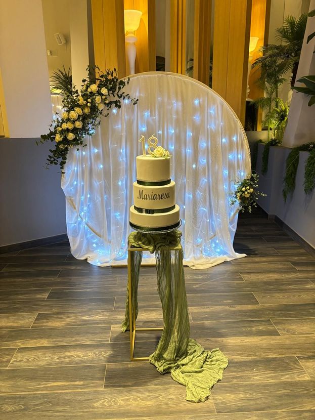 Una torta è appoggiata su un tavolo davanti a una tenda bianca con delle luci.