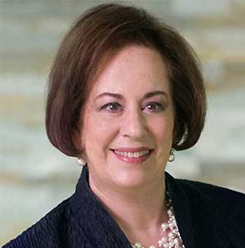 A woman wearing a black jacket and pearls is smiling for the camera.