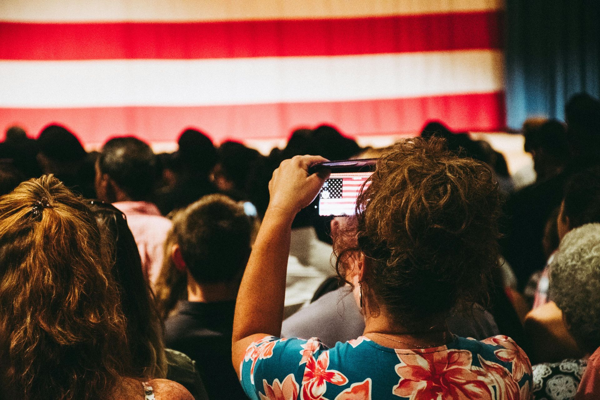 A woman is taking a picture of an american flag with her cell phone.