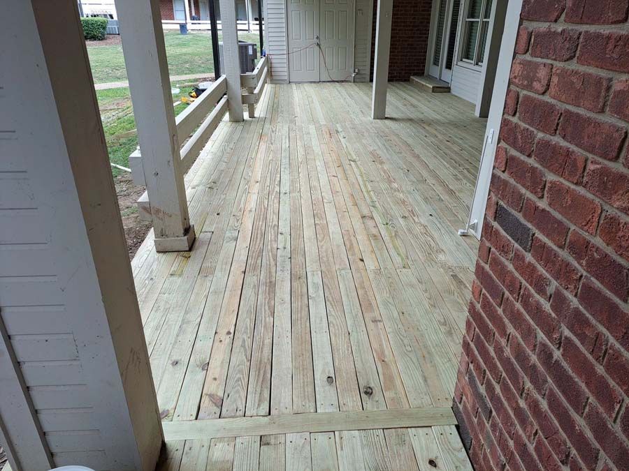 A wooden porch with a brick wall in the background.
