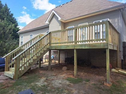 A wooden deck with stairs leading up to it is in the backyard of a house.