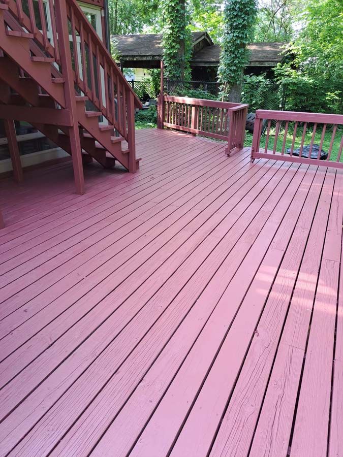 A red wooden deck with stairs and a house in the background.