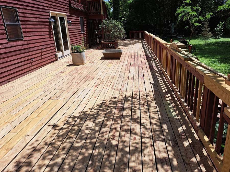 A large wooden deck with a railing in front of a red house.