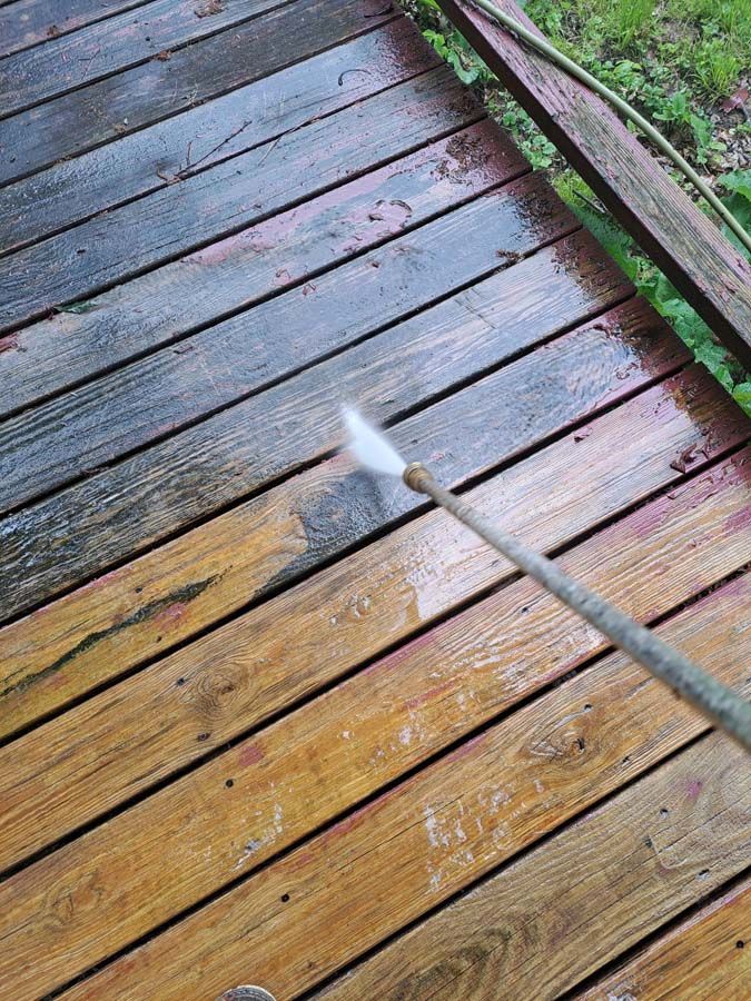 A person is using a high pressure washer to clean a wooden deck.