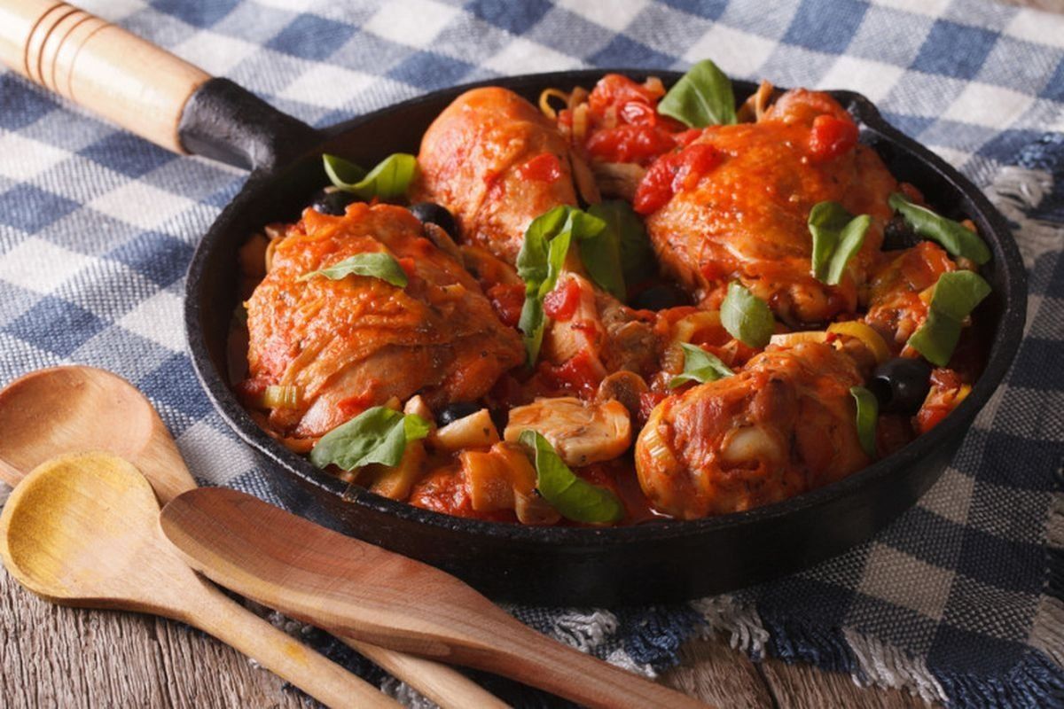 Padella di pollo in salsa con peperoni su una tovaglia a quadri, con cucchiai di legno a portata di mano.