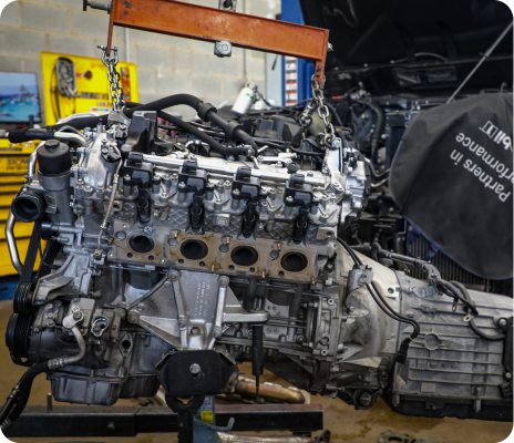 Car engine and transmission on a workshop pallet, with tools and a yellow machine in the background. | Trask Automotive