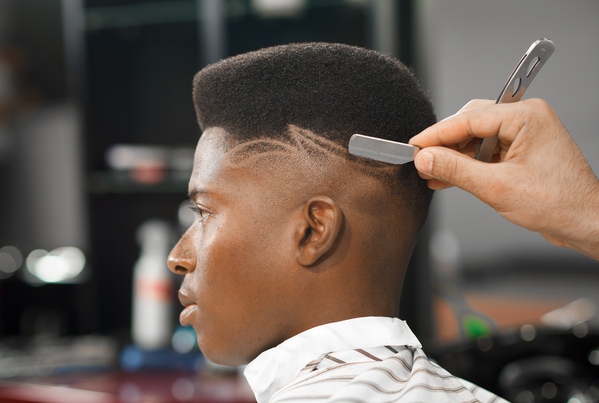 A man is getting his hair cut by a barber with a razor.