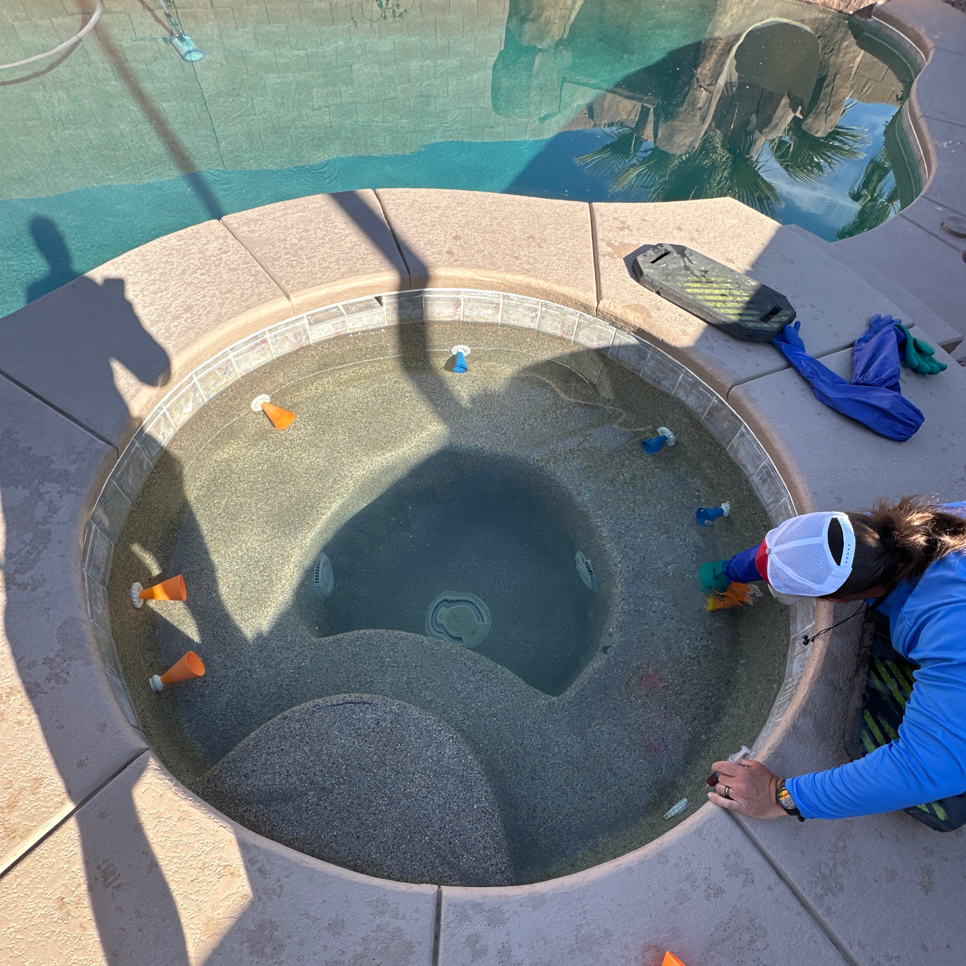 Person beside an empty circular hot tub, with scattered toys and a blue towel on the deck.