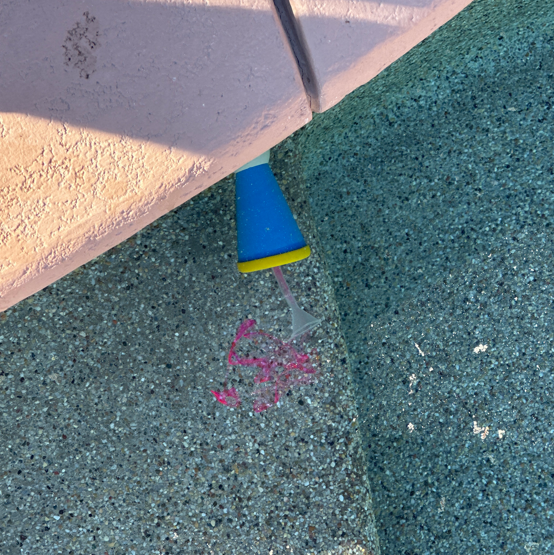 Blue-and-yellow cone on pavement beside a curb with pink chalk markings