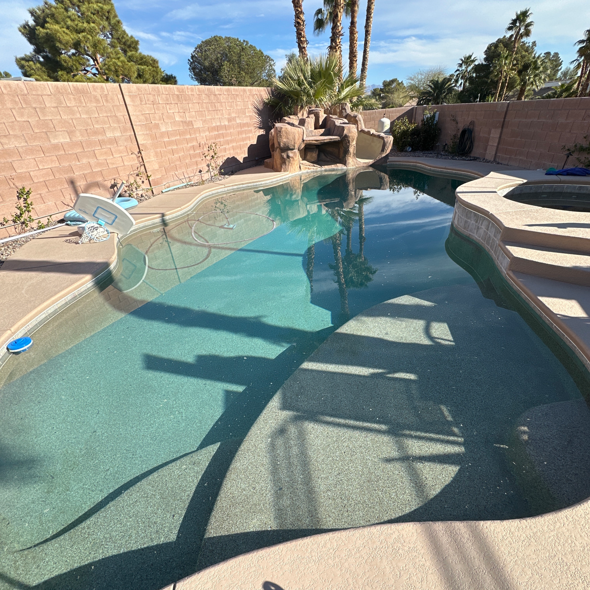 Backyard swimming pool with rock waterfall, turquoise water, and desert landscaping under bright sun